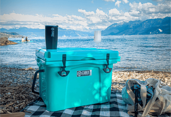 A Cubix Outdoor 25 Quart Viva Cooler with a Cubic tumbler next to a lake
