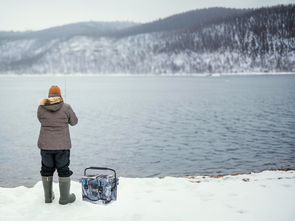 Person surrounded by white snow standing and fishing by a lake.