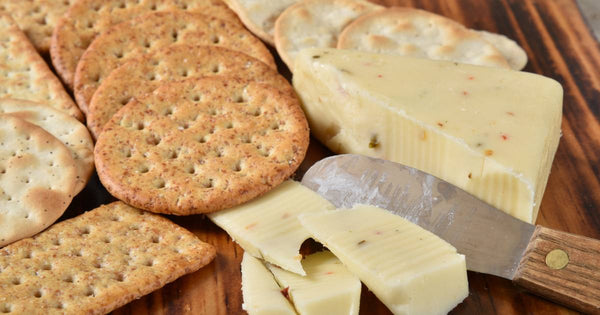 Cheese and crackers on a wooden board with a cheese knife.